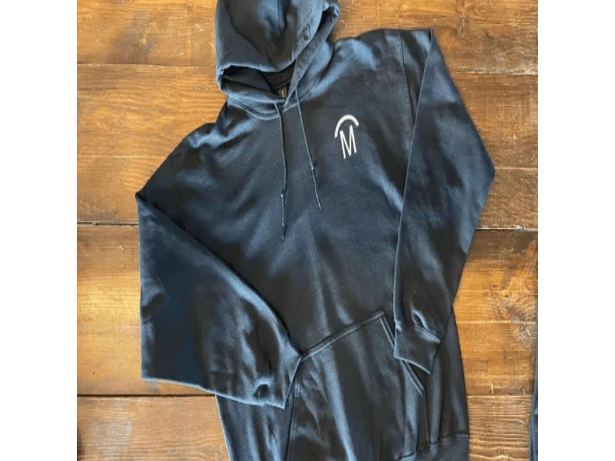 Black hoodie with white logo on wooden surface.